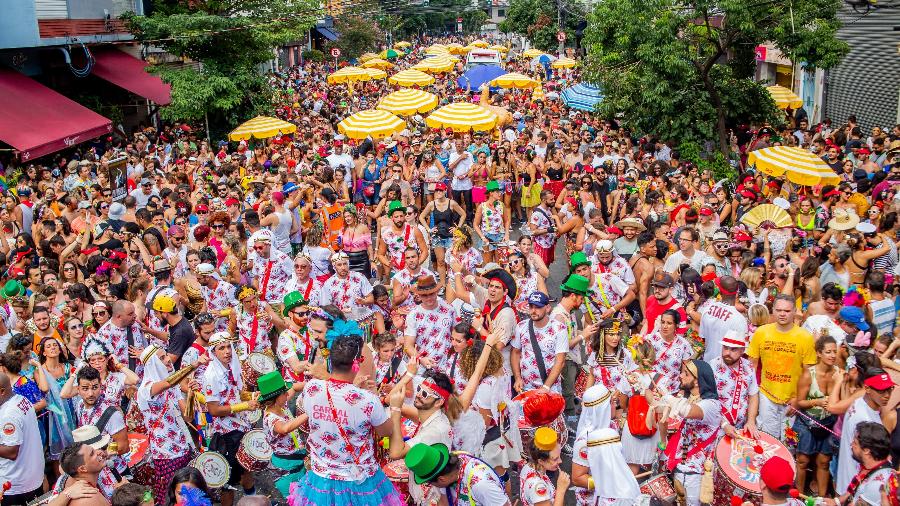 Bloco de rua em São Paulo durante o Carnaval, com foliões animados ocupando as ruas, vestidos com fantasias coloridas e celebrando ao som da música.